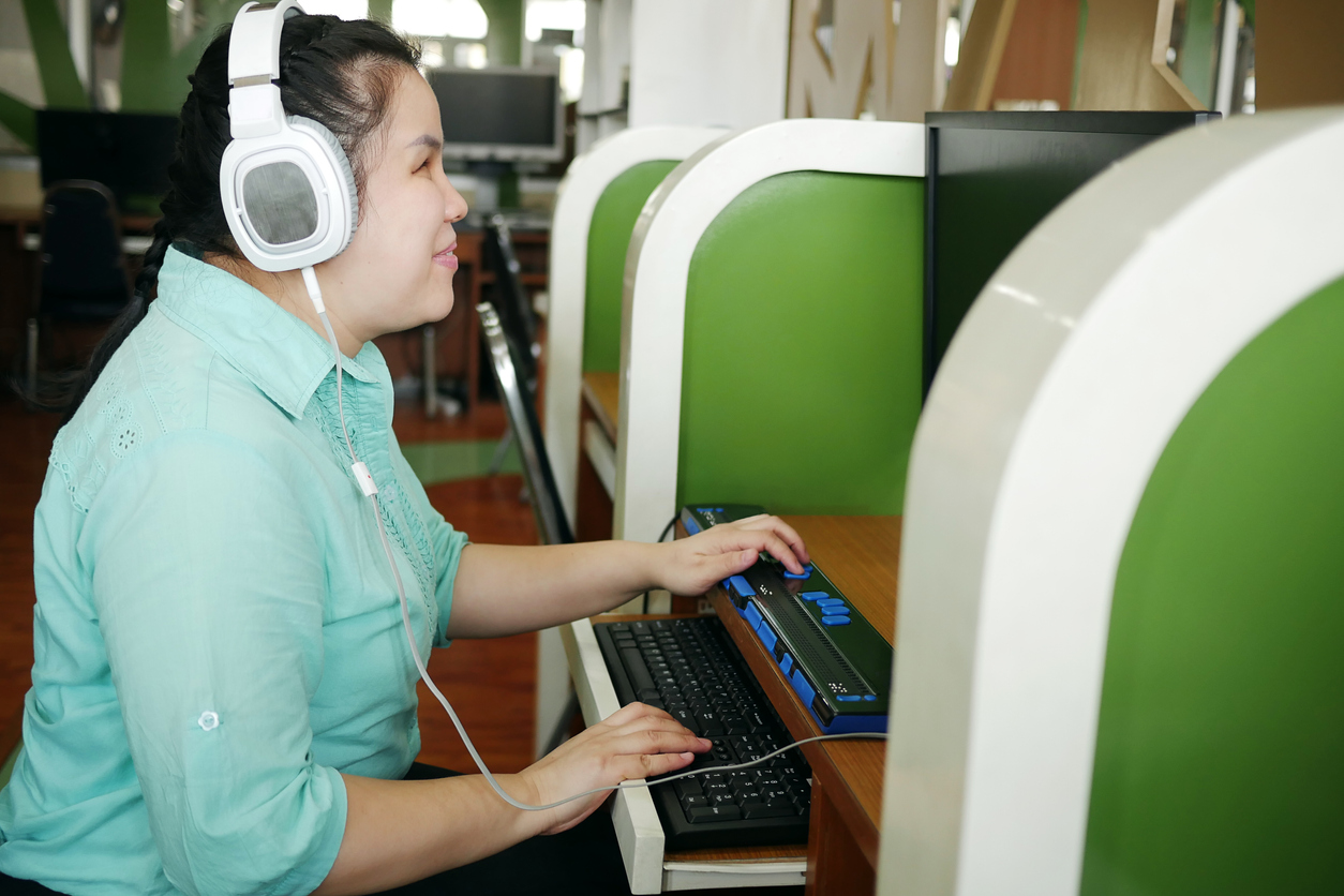 Mulher asiática com cegueira usando computador com display braille atualizável ou terminal braille, um dispositivo de assistência tecnológica para pessoas com deficiência visual no local de trabalho.