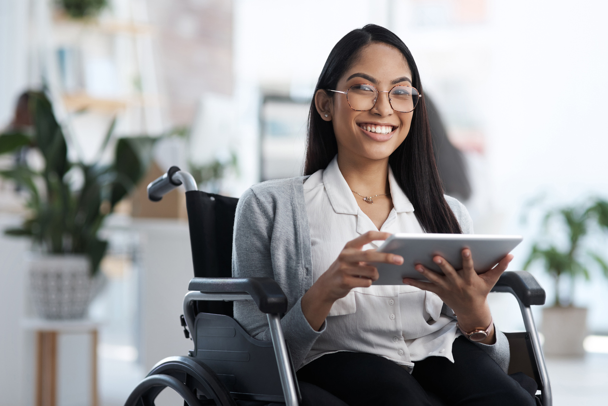 Uma jovem empresária em uma cadeira de rodas usando seu tablet no escritório.