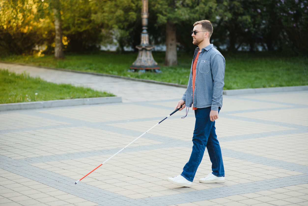 Homem cego andando na calçada segurando a bengala.