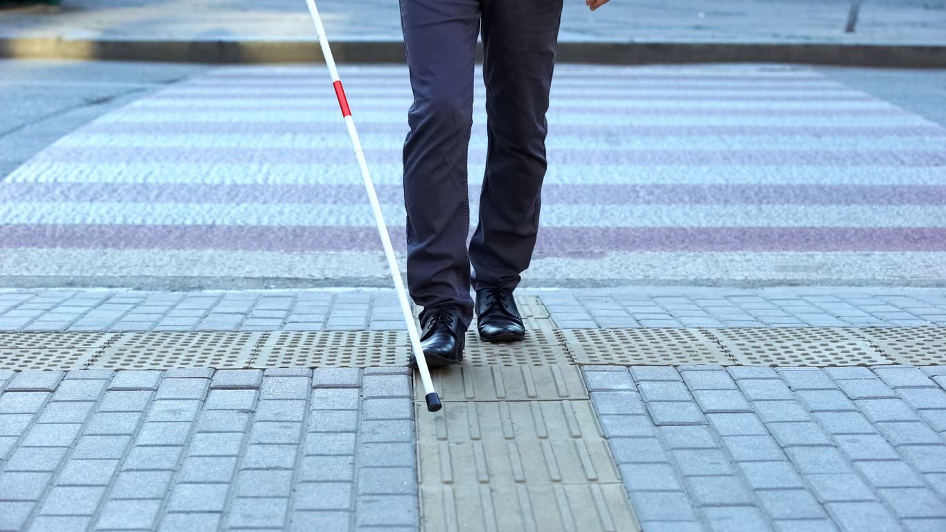 Homem com deficiência visual usando ladrilhos táteis para andar pela cidade.