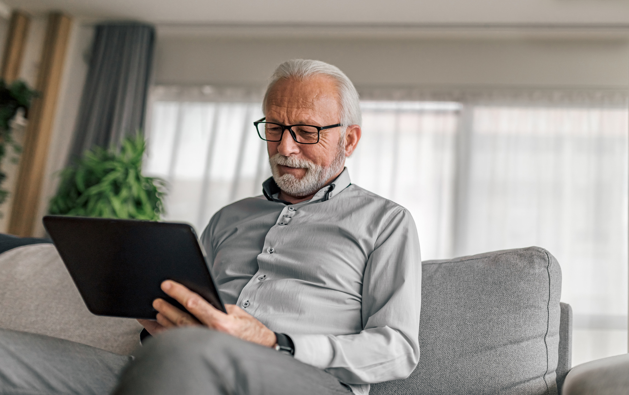 Profissional idoso masculino sorridente usando tablet digital enquanto está sentado no sofá.